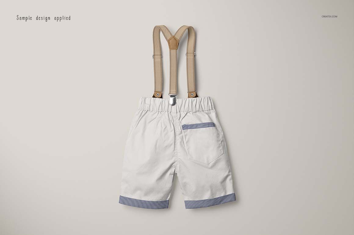 White boys shorts with blue striped accents and tan suspenders, displayed in a flat lay mockup on a neutral surface.