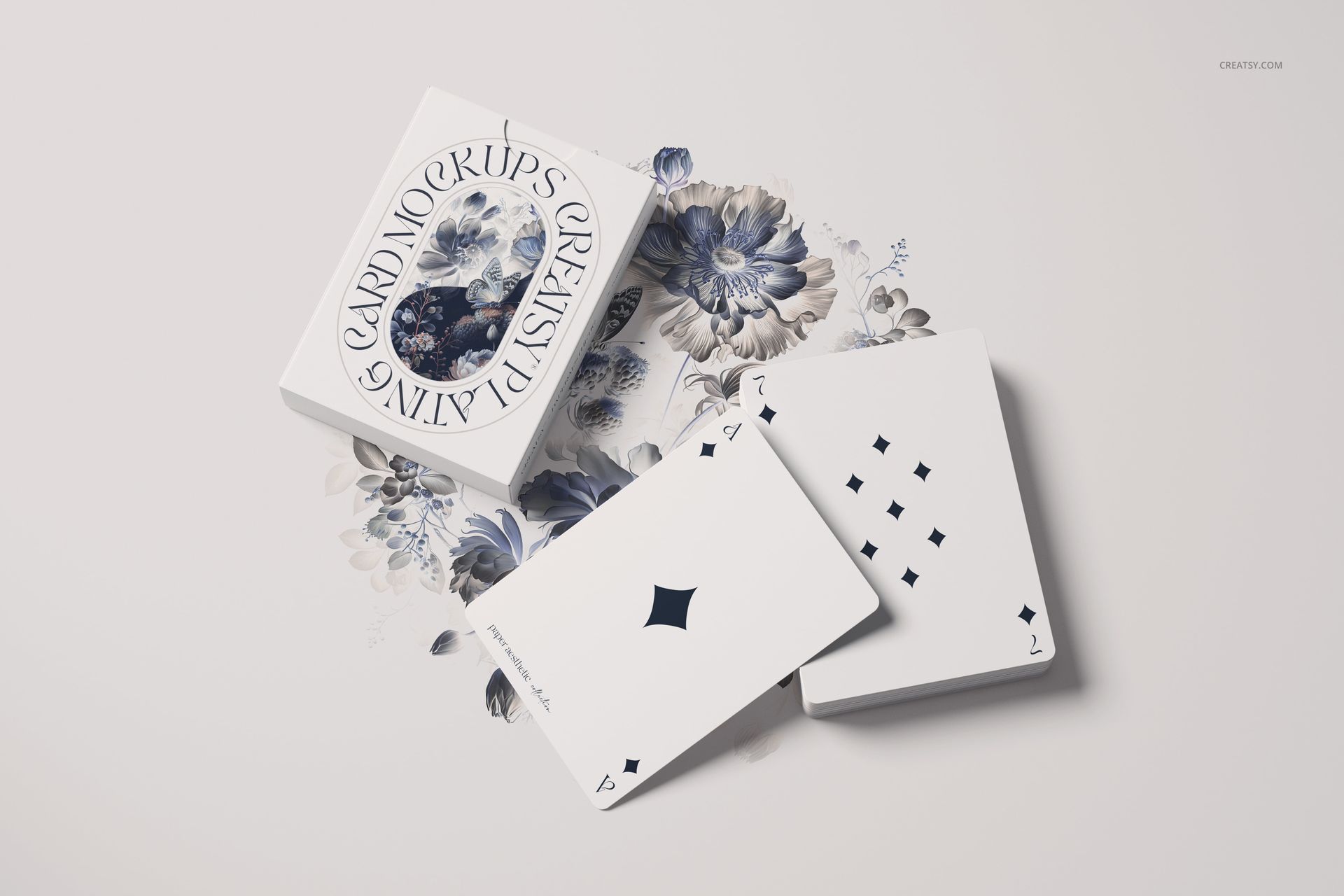 Playing cards mockup set featuring a deck and two cards on a white surface with blue floral illustrations underneath.