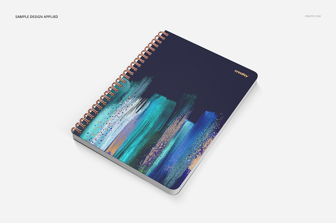 Notebook mockup with copper spiral binding and square holes, dark cover with colorful paint strokes, top perspective.