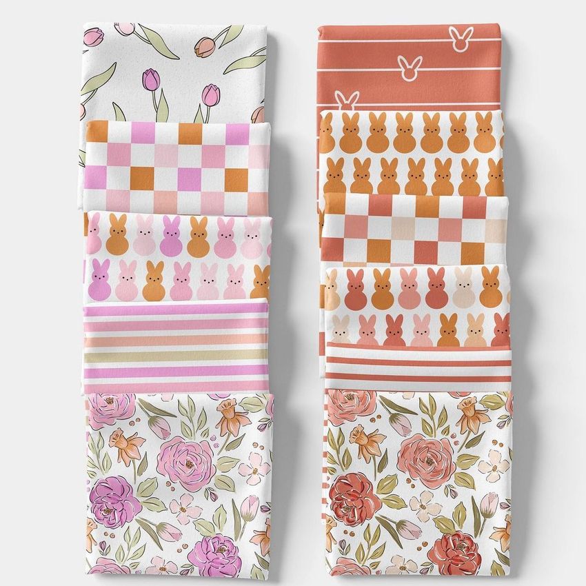 Folded fabrics mockup showing two neat stacks of patterned textiles with floral, bunny, and checkered designs in pastel colors.