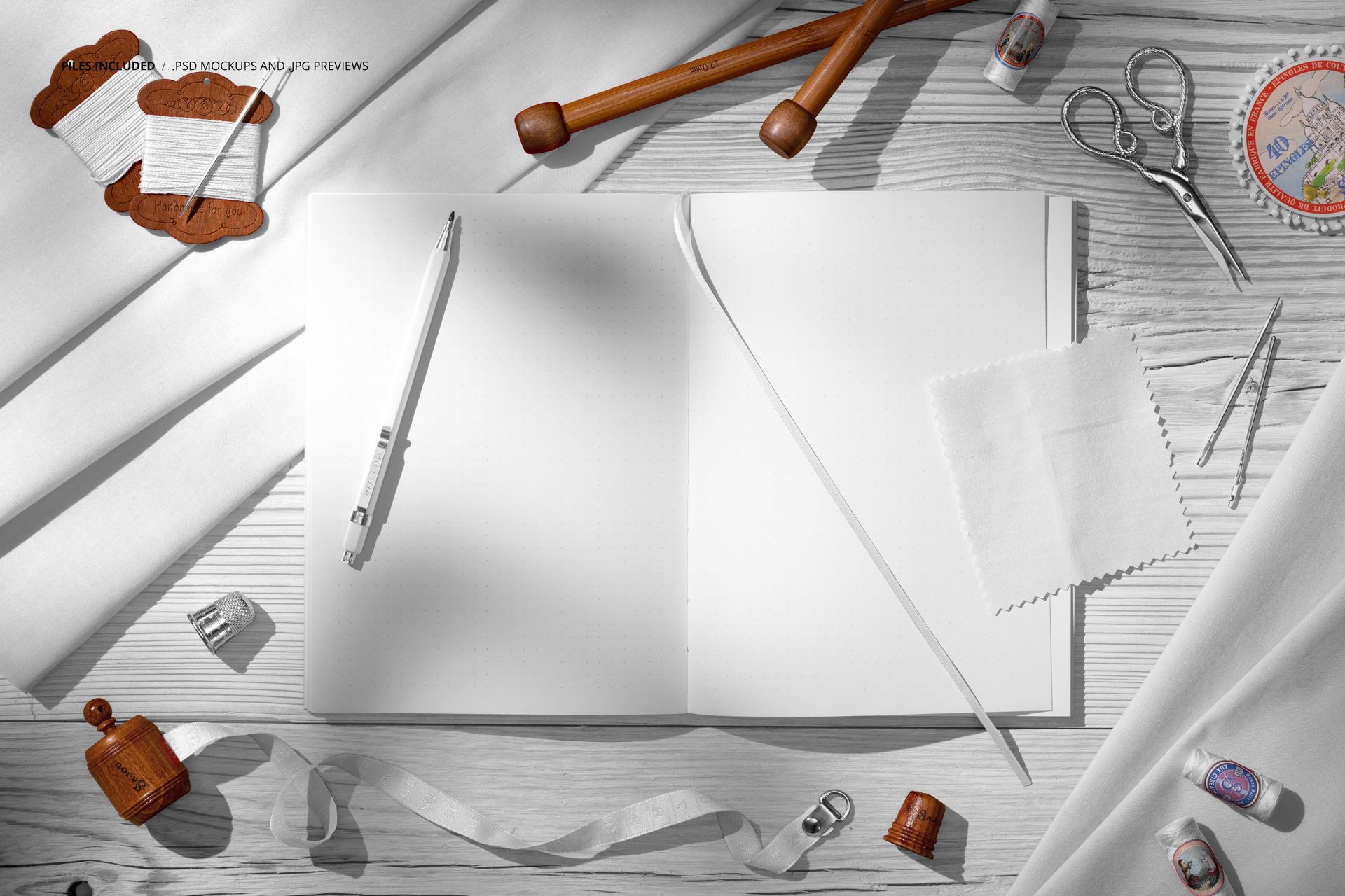 Top view of a creative desk with white cotton fabrics, open blank notebook, pen, scissors, and sewing props.