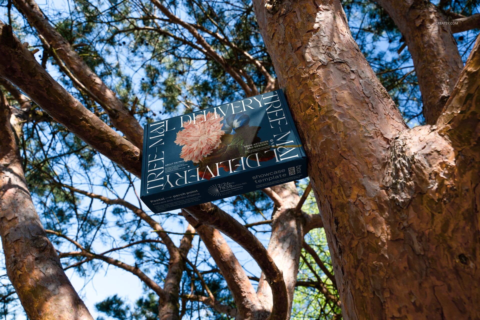 Mailing box mockup featuring a dark floral pattern, placed on tree branches with sunlight and green foliage.