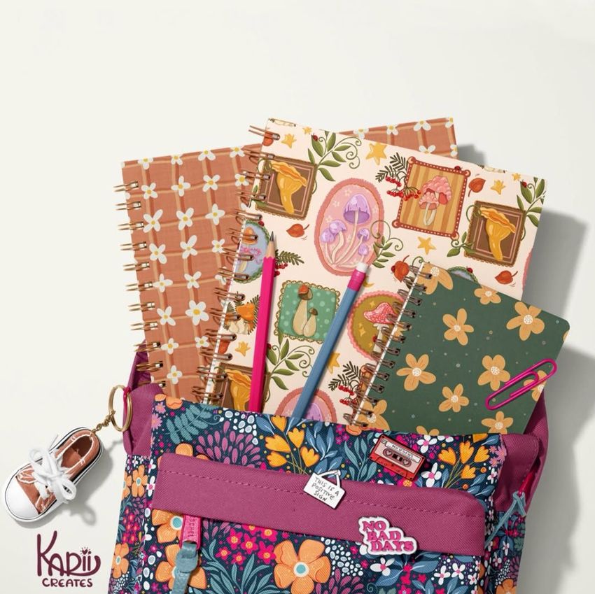 School backpack mockup with spiral notebooks featuring colorful floral and mushroom patterns, viewed from above on a light background.