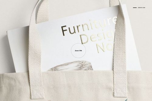 Front view of a beige polyester tote bag mockup with sturdy handles, holding a magazine with gold text.