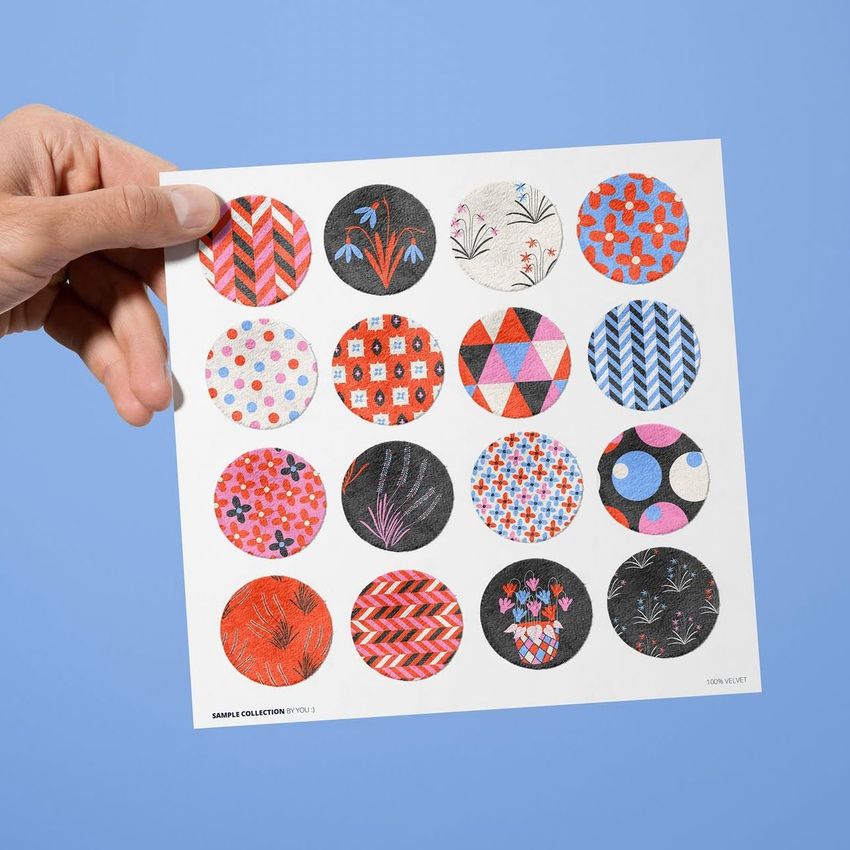 Hand holding a velvet swatches card mockup featuring sixteen colorful patterned fabric circles on a light blue background.