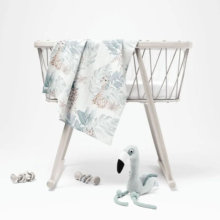 Crinkle muslin swaddle blanket mockup draped over a modern baby bassinet, featuring a soft giraffe pattern and pastel colors.