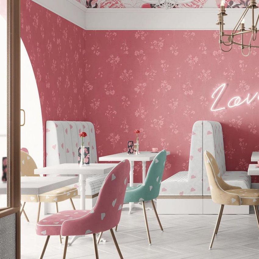 Cafe interior wallpaper mockup showing pink patterned wallpaper, pastel chairs with heart designs, and white tables in a cozy setting.