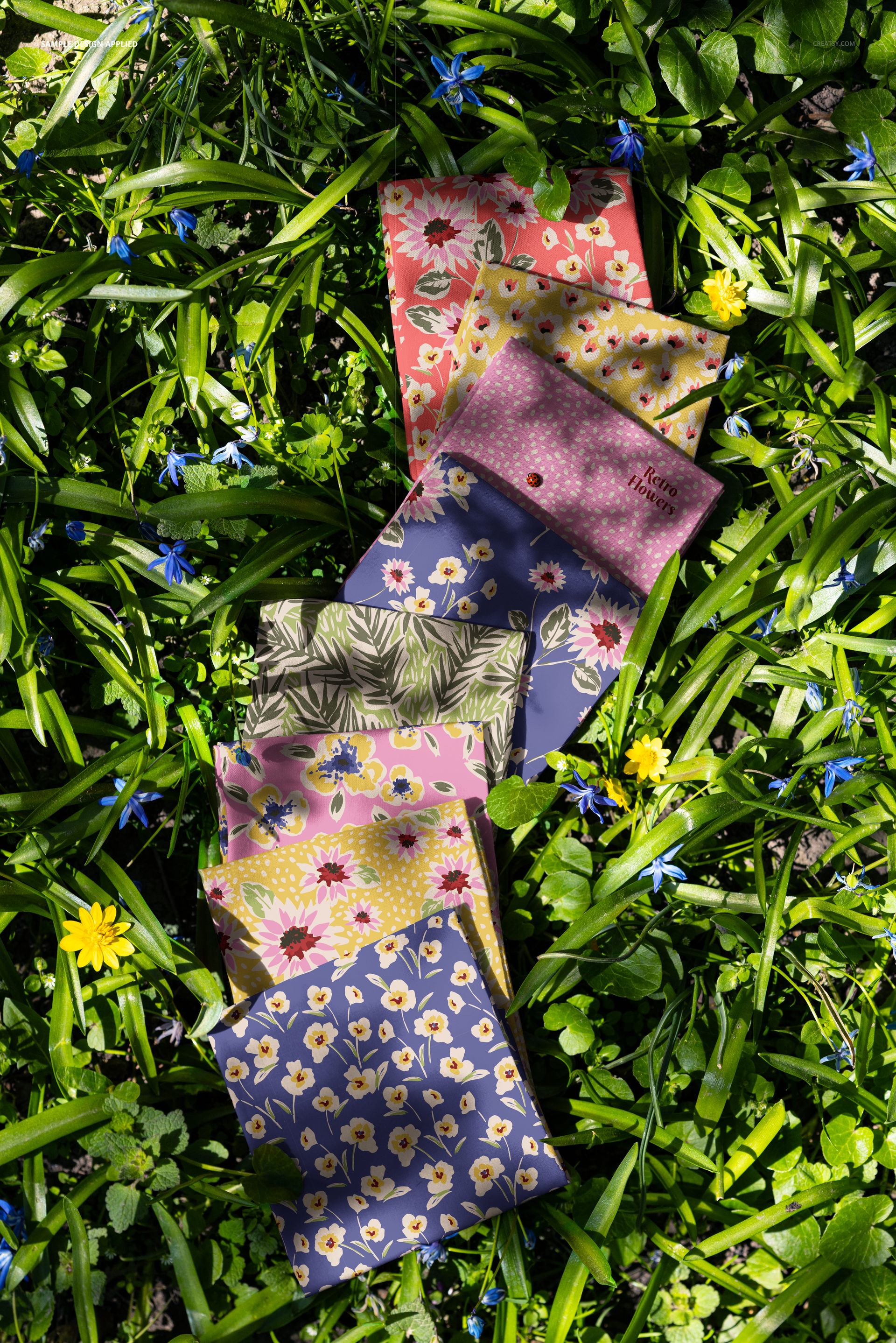 PSD mockup showing a top view of multiple decorative fabric samples placed on natural meadow grass among wildflowers.