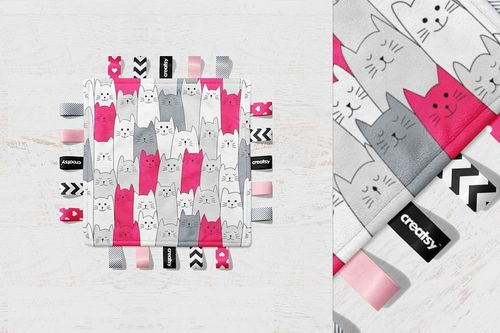 Taggie blanket mockup featuring a square blanket with pink, gray, and white cat pattern and assorted fabric tags.