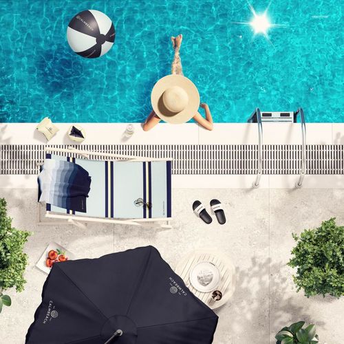 Overhead perspective of a poolside setup featuring a striped towel mockup, sun hat, sandals, and blue water.