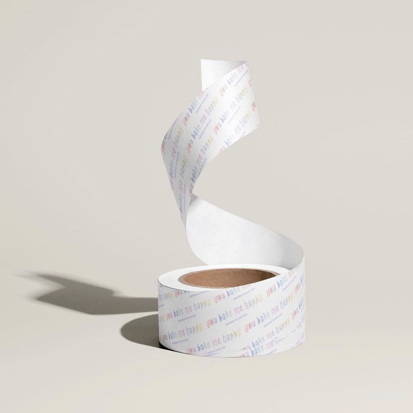 Packaging tape mockup featuring a roll of white paper tape with pastel text, unspooled in a spiral on a light beige background.