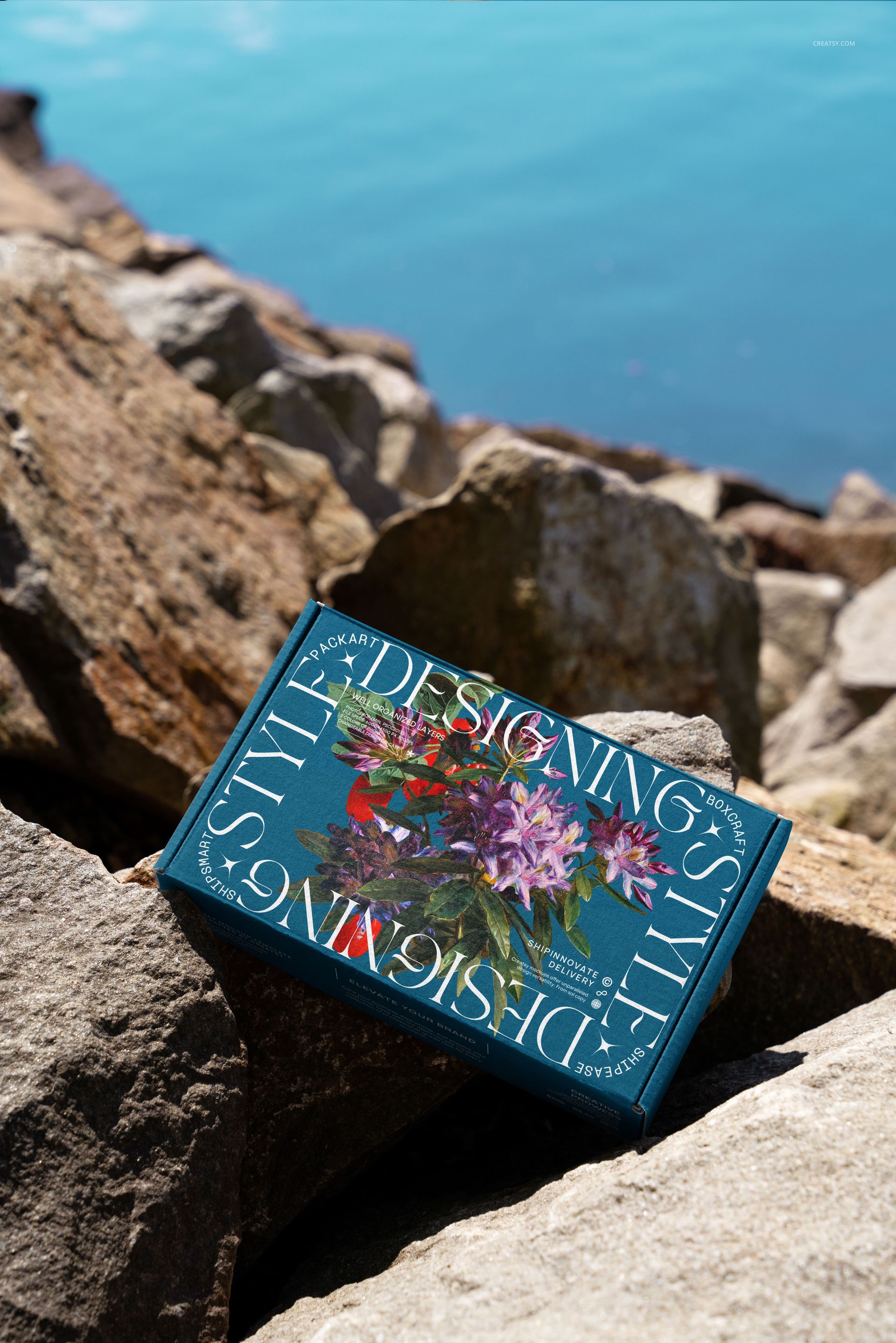 PSD mockup of a mailing box featuring botanical artwork and bold lettering, set among rocks by the seaside.