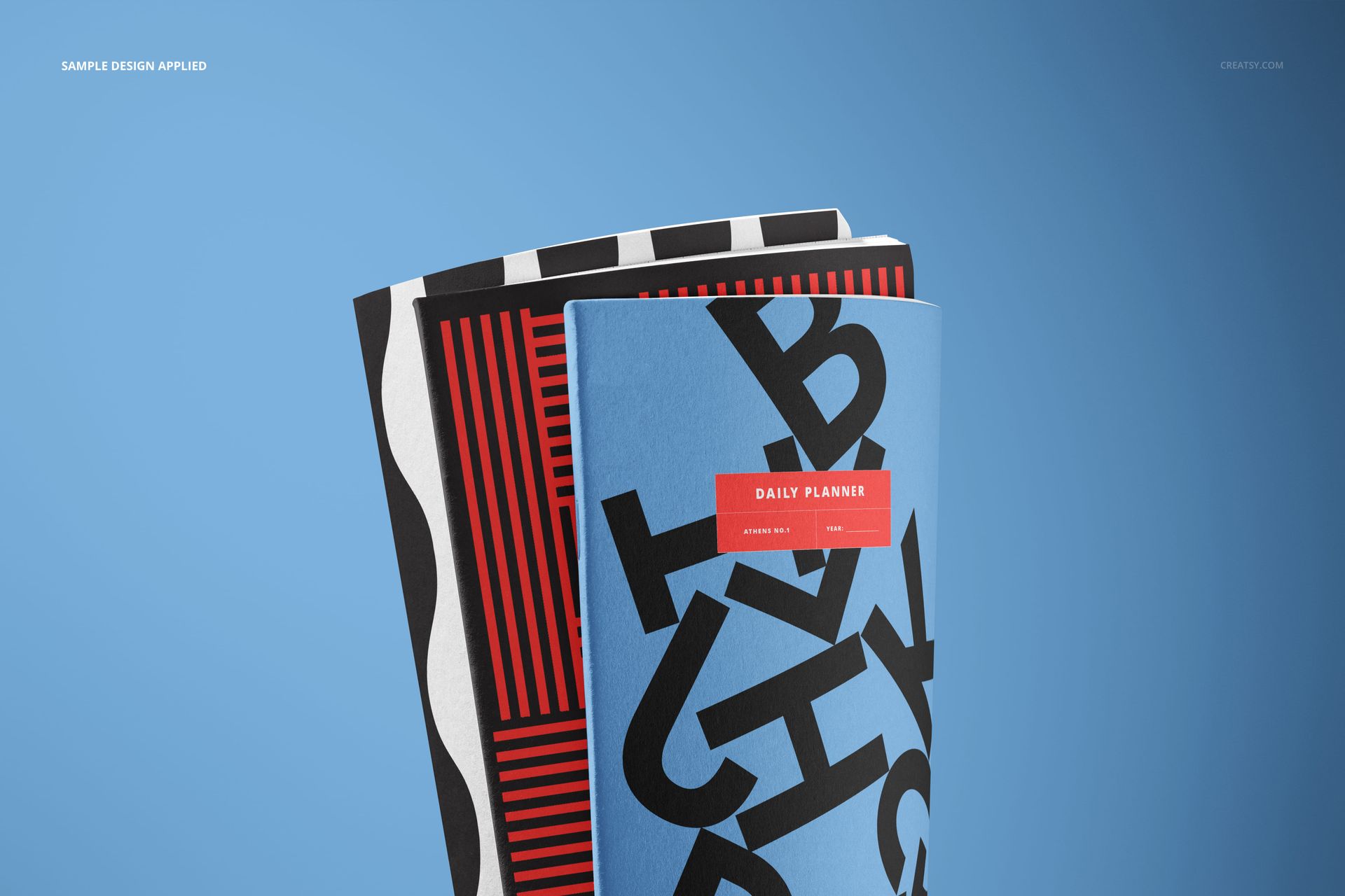 PSD mockup displaying three upright notebooks with colorful abstract covers, set against a solid blue background.