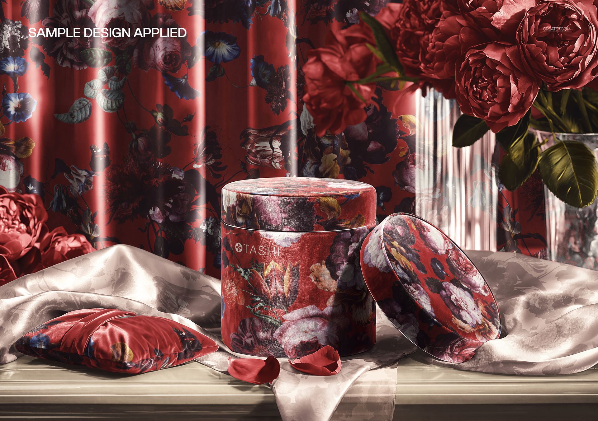 PSD mockup of a cylindrical gift box with red floral wrapping paper, shown with matching pillow and petals.