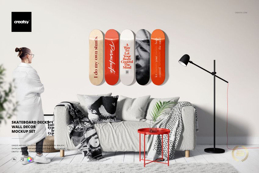 PSD mockup showing skateboard decks with varied patterns arranged above a couch, with a person standing nearby.