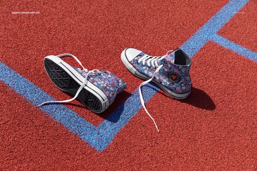 Pair of high-top sneakers with colorful floral pattern placed on a red outdoor track with blue lines, side view.