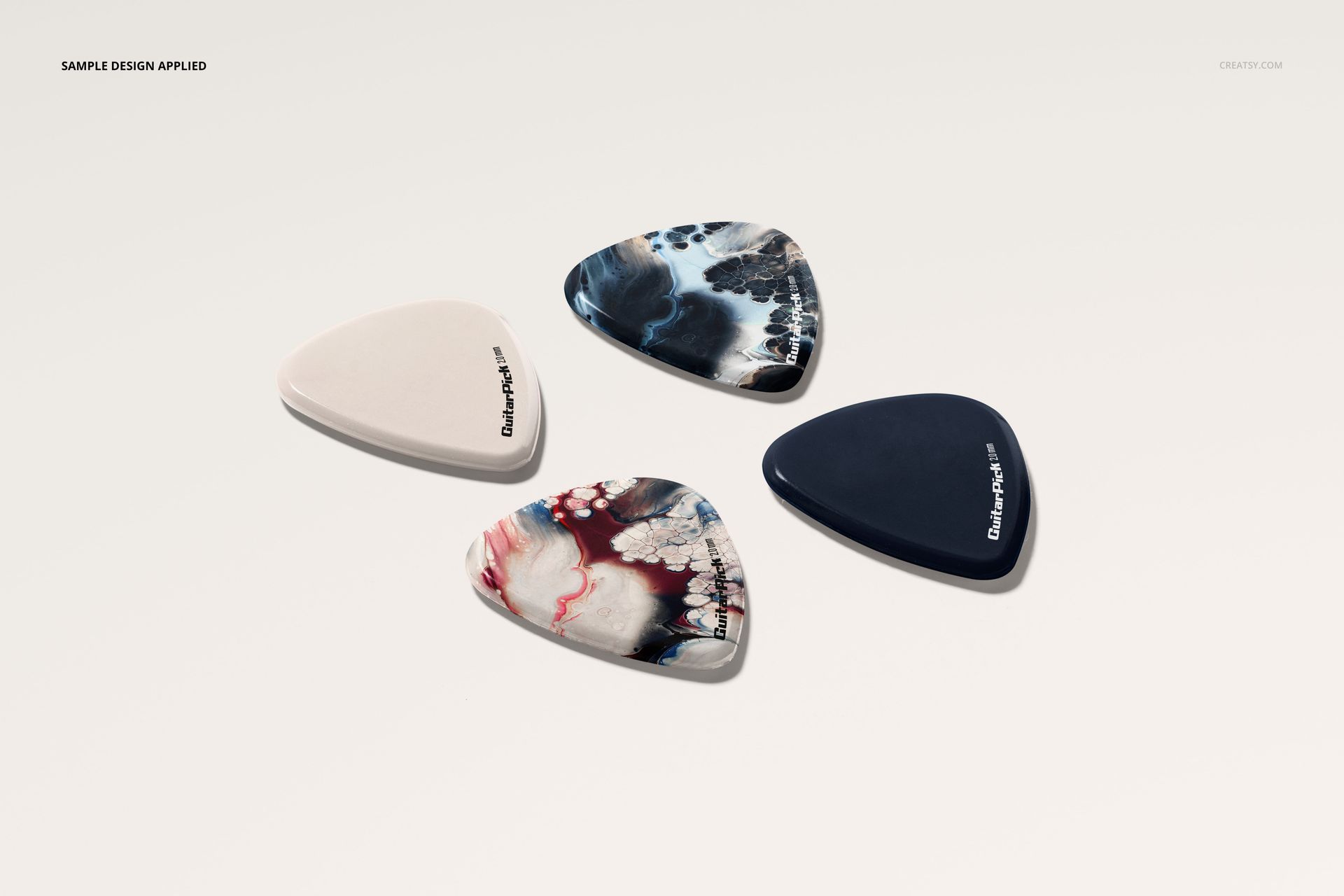 Guitar pick PSD mockup showing four picks with unique designs and colors, laid out on a pale surface from overhead.