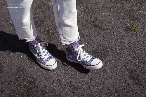 Outdoor scene with a pair of mockup sneakers decorated in multicolored patterns, viewed from above on rough ground.