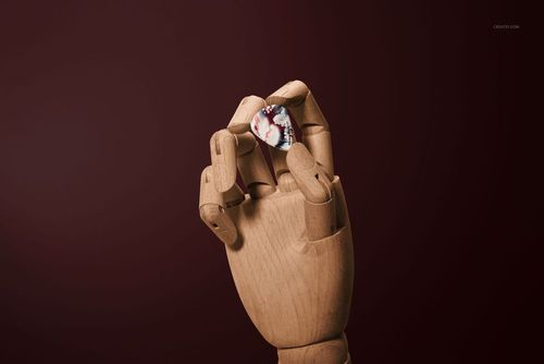 Guitar pick in a wooden articulated hand, featuring a marbled design, presented in a PSD mockup scene.