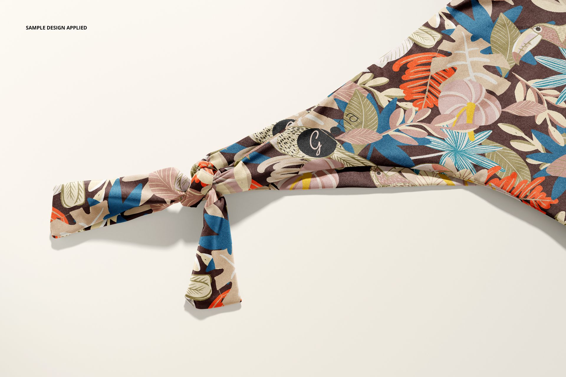 Bikini mockup showing side tie detail, decorated with vibrant leaves and flowers in blue, pink, and beige tones.