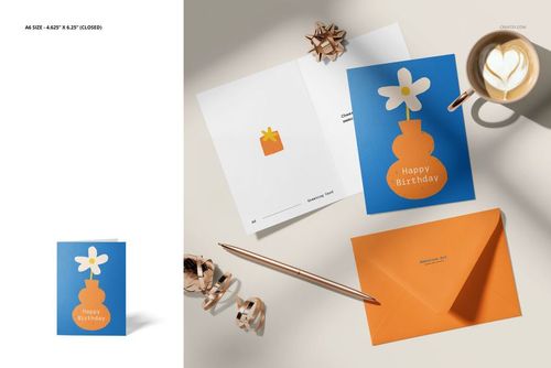 Greeting card mockup set showing an open and closed card with floral design, orange envelope, pen, ribbon bows, and latte art from a top view.