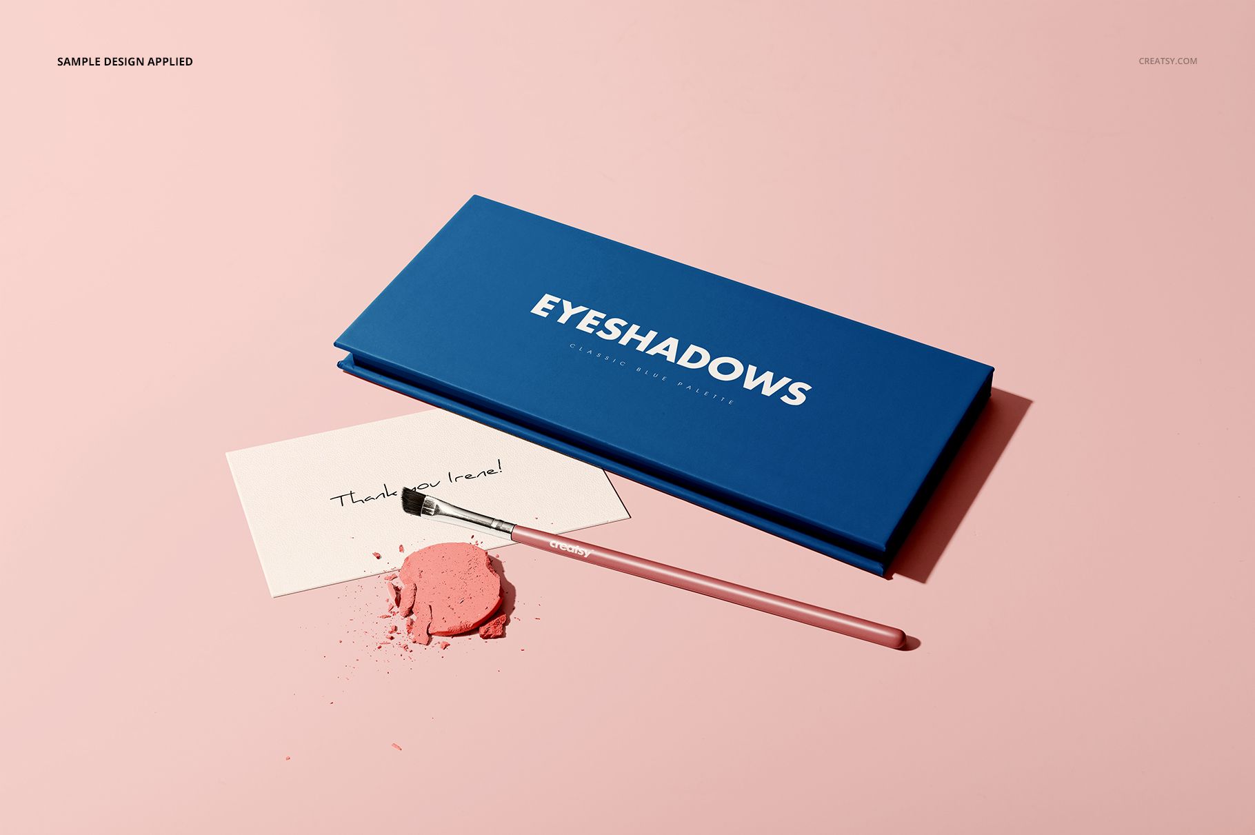 Blue eyeshadow palette mockup set displayed with a makeup brush and scattered pink eyeshadow on a light pink background.