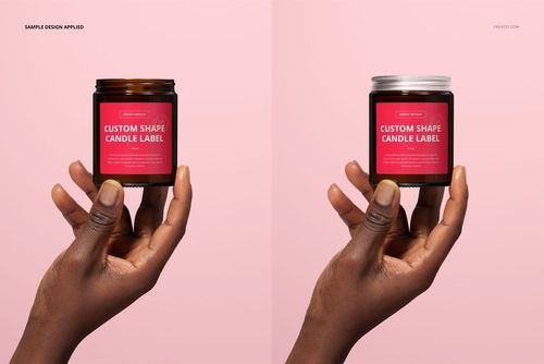 PSD mockup featuring an amber glass candle jar with custom red label, held by hand, displayed on a pale pink surface.