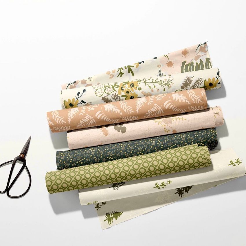 Fabric rolls mockup showing six patterned fabric rolls in earthy tones, arranged on a white surface with scissors nearby.