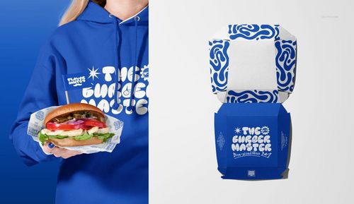 Close-up of a vegan burger with lettuce, tomato, and onion in blue branded wrapper, beside a blue burger box mockup.