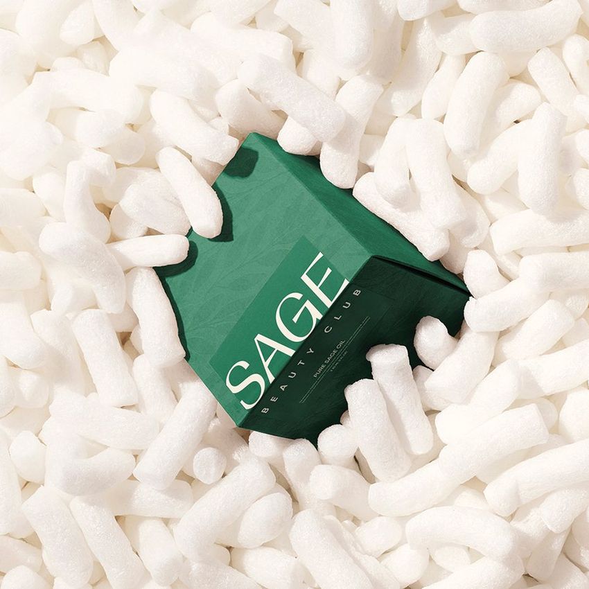 Green packaging box with bold white text partially covered by white packing peanuts, viewed from above in a sticker mockup scene.