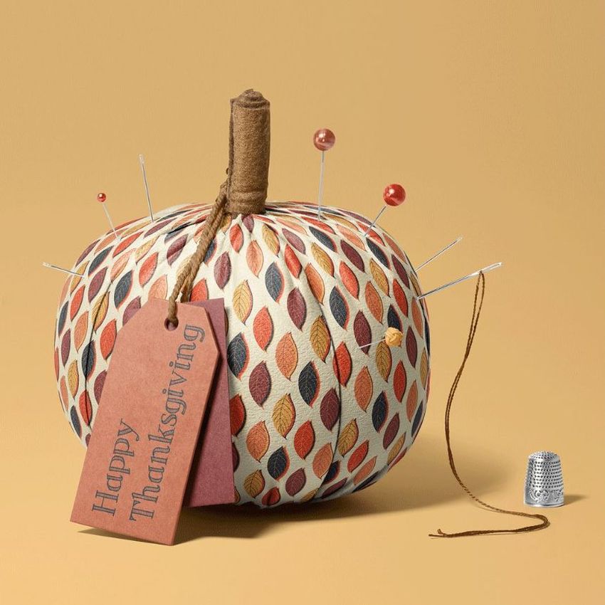Fabric pumpkin mockup with a patterned surface, sewing pins, a brown stem, and a tag reading Happy Thanksgiving on a beige background.