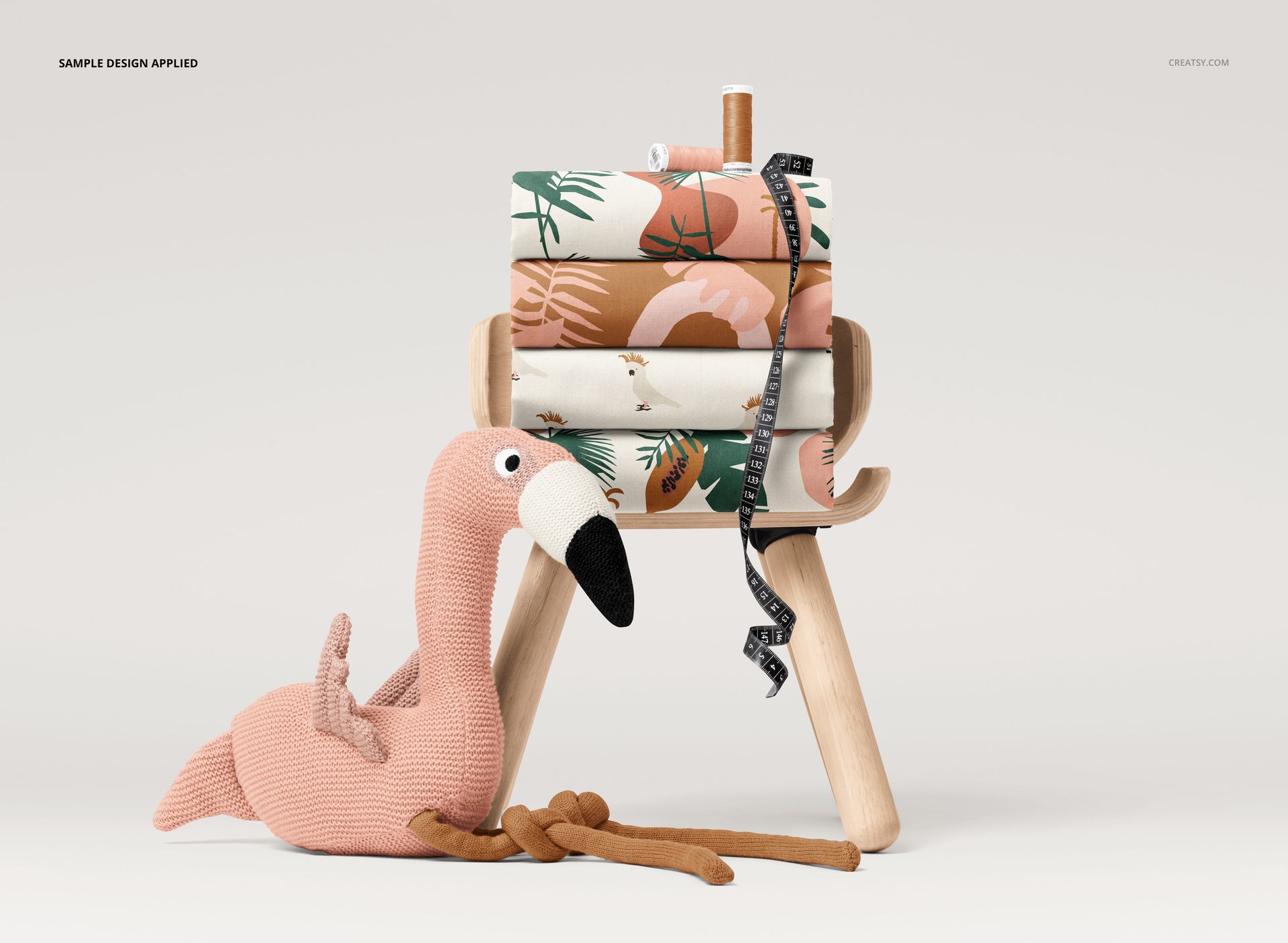 PSD mockup showing a pile of folded fabrics with various designs, a measuring tape, thread spool, and a soft flamingo plush.