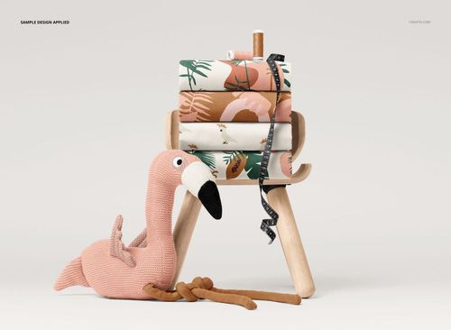 PSD mockup showing a pile of folded fabrics with various designs, a measuring tape, thread spool, and a soft flamingo plush.