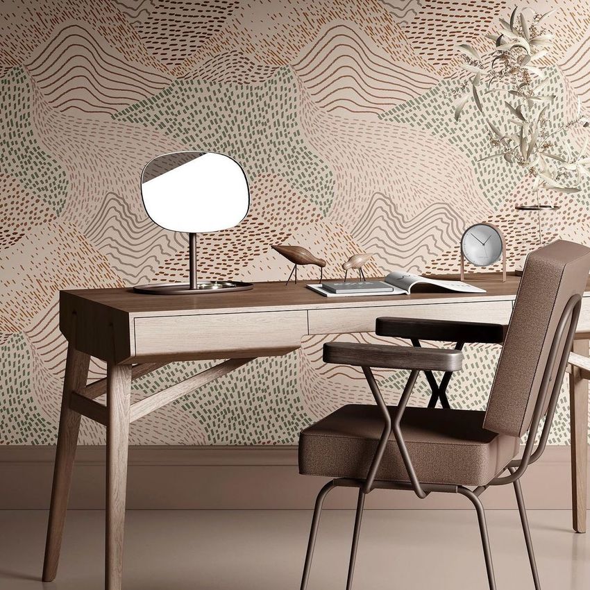 Interior scene with a wooden desk mockup, brown chair, mirror, clock, and decorative bird figures against a patterned wall.