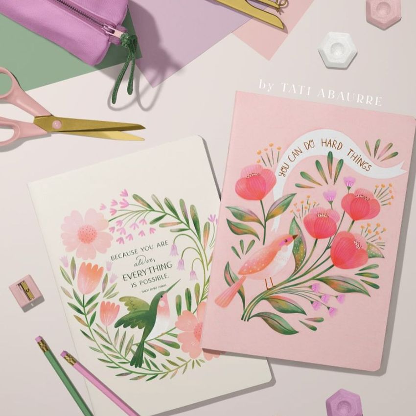 Stationery mockup featuring two A4 notebooks with illustrated floral and bird covers, surrounded by pastel office supplies.