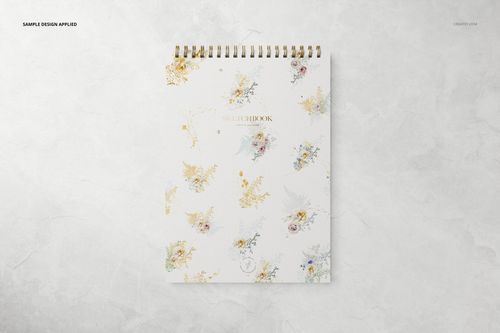 Top-down perspective of a stationery mockup showing a sketchbook with gold spiral binding and pastel flower illustrations on the cover.