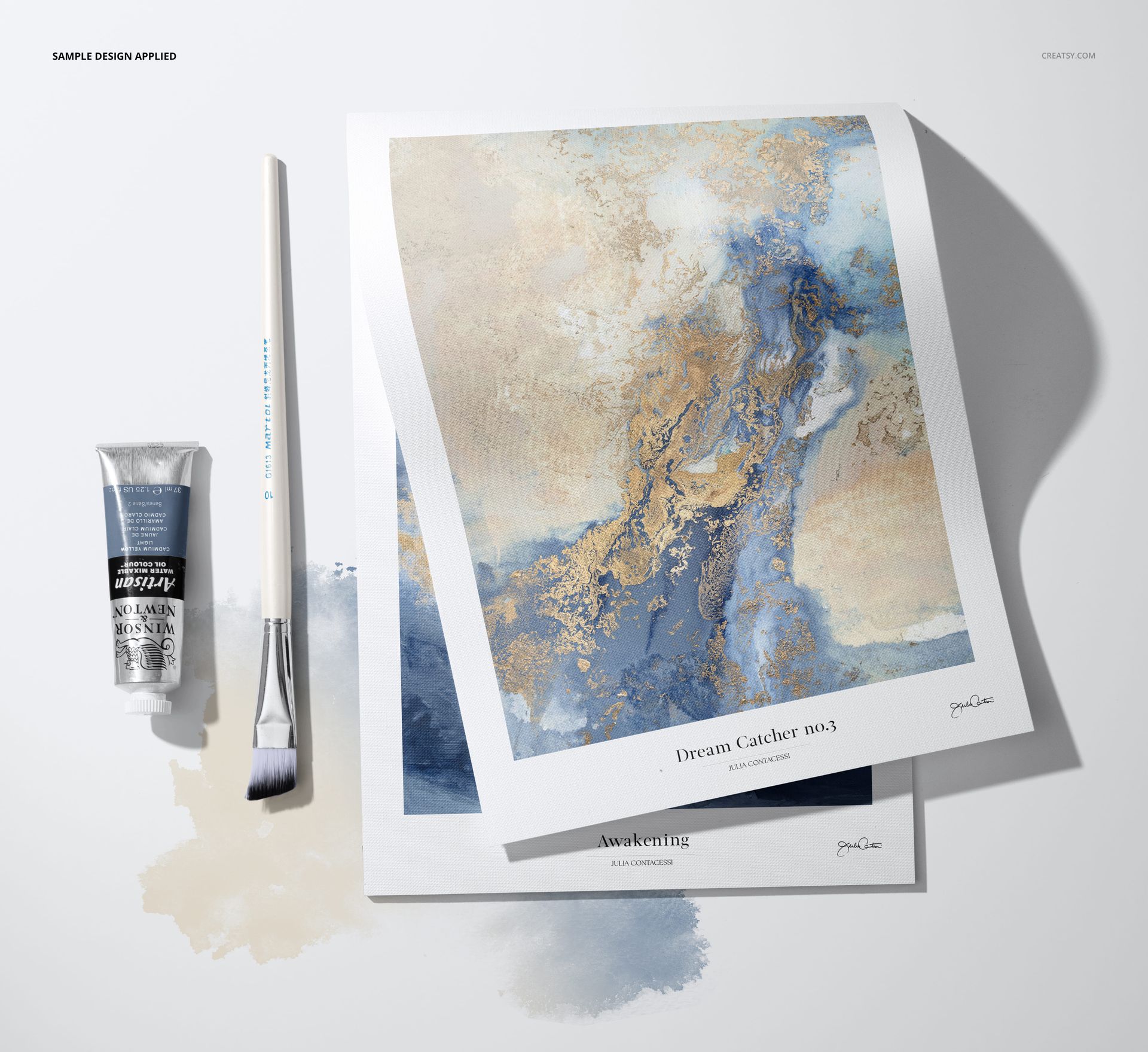 Top view of decorative paper pad mockup with abstract blue and gold artwork, paintbrush, and paint tube on white surface.