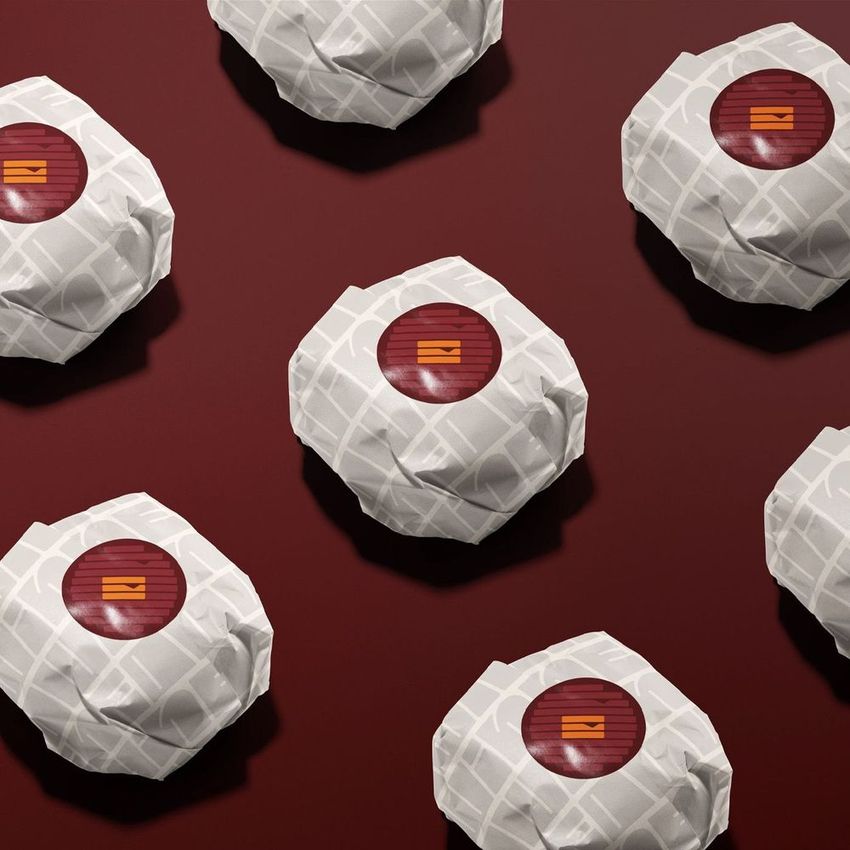 Burger mockup featuring multiple wrapped burgers on a deep red background, each with patterned white paper and a red sticker.