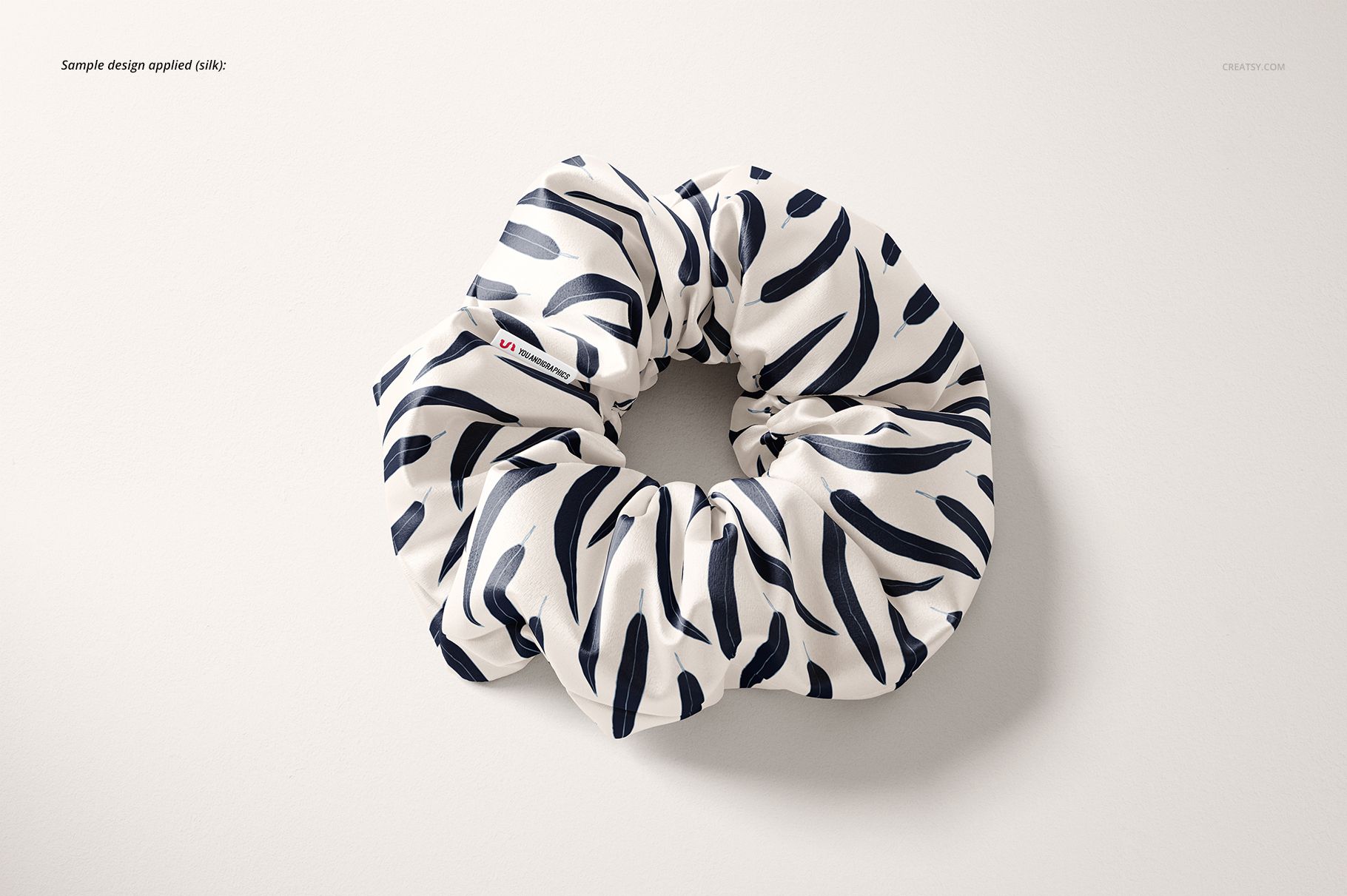 Top view of a mockup hair scrunchie featuring a white fabric with dark blue curved lines on a neutral surface.