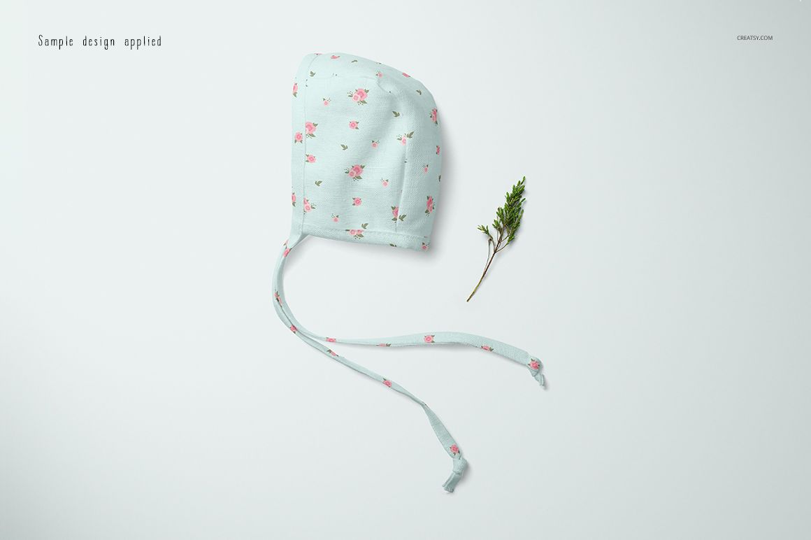 Baby bonnet mockup featuring a soft blue fabric with delicate pink flowers, displayed flat beside a sprig on white background.