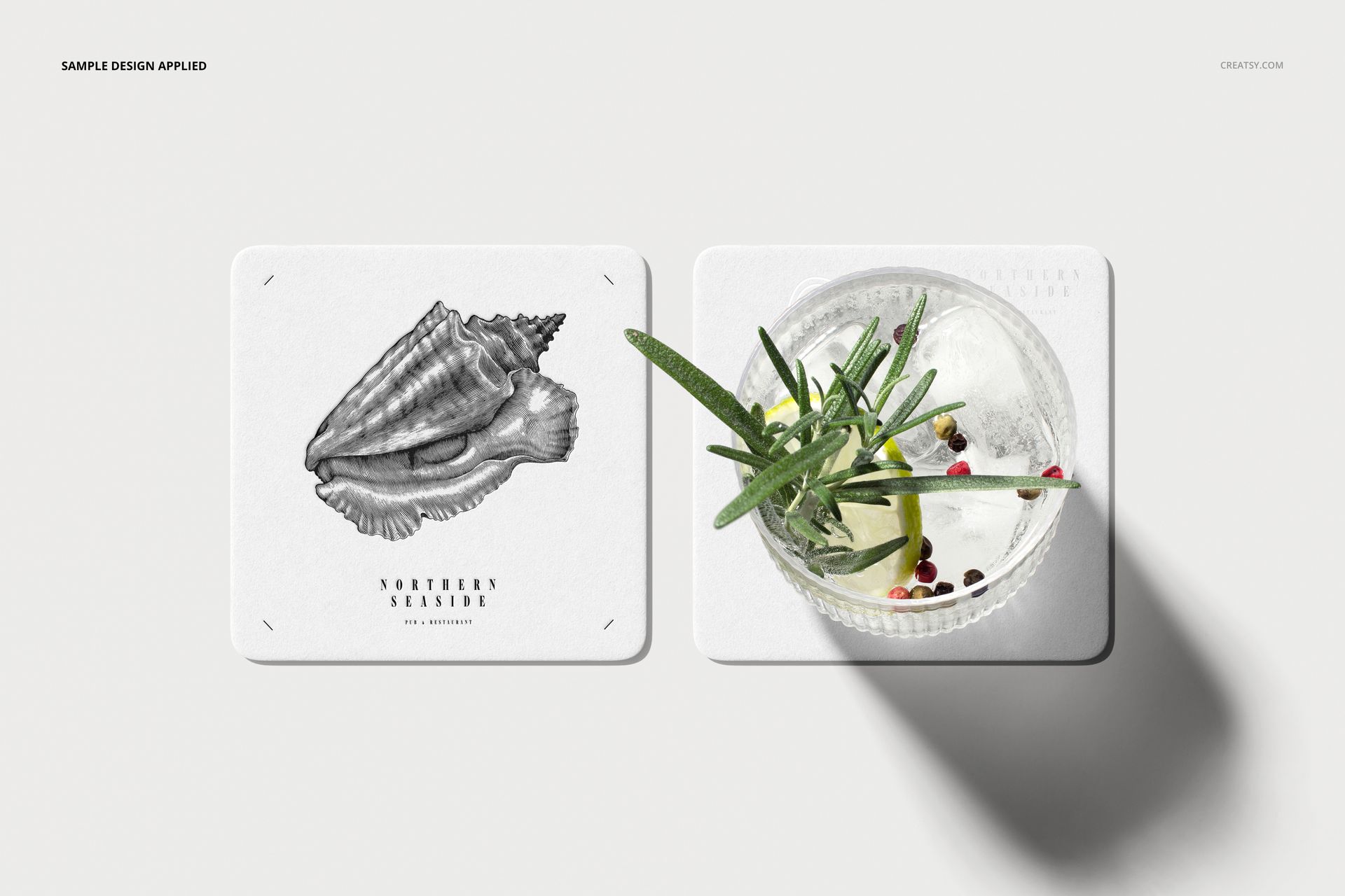 Square coasters mockup set featuring a shell drawing on one coaster and a glass with garnish on the other, viewed from above.