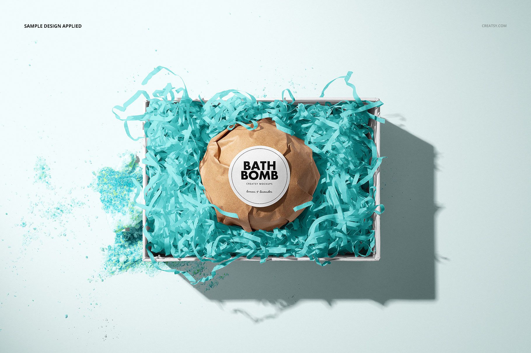 Bath bomb mockup in a rectangular box filled with blue paper shreds, viewed from above on a light background.