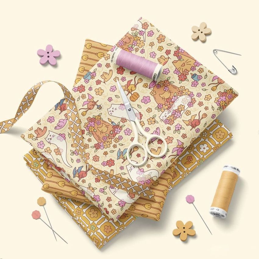 Folded jersey fabric mockup featuring floral and animal patterns, arranged with ribbon, scissors, thread spools, and sewing pins.