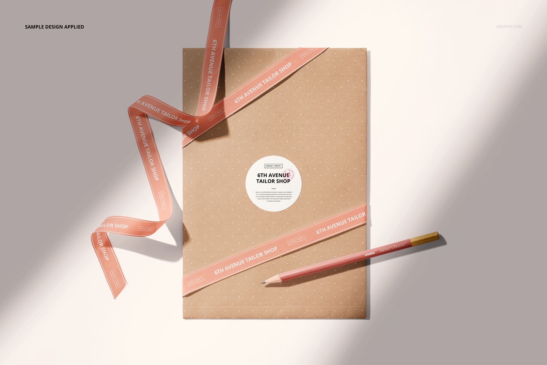 Shipping envelope mockup with dotted pattern, round sticker, pink ribbon, and pencil on a light surface, top view.