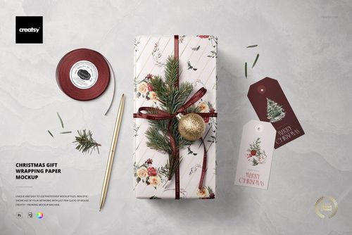 Neatly wrapped present with festive floral wrapping paper, fir branches, gold ornament, ribbon, and holiday tags in a PSD mockup.