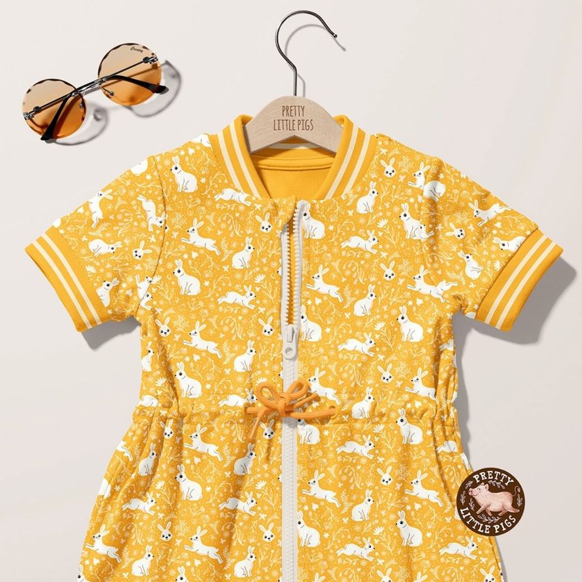 Baby dress mockup featuring a yellow short-sleeve garment with white bunny and floral pattern, displayed on a wooden hanger.