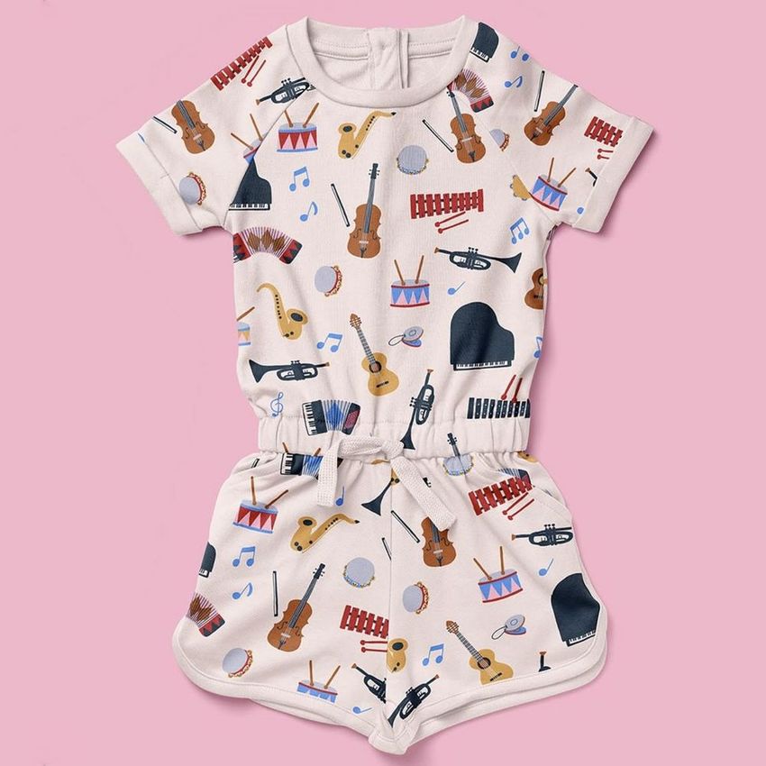 Girls cotton playsuit mockup featuring a musical instrument pattern with colorful illustrations on a light fabric, displayed on a pink background.