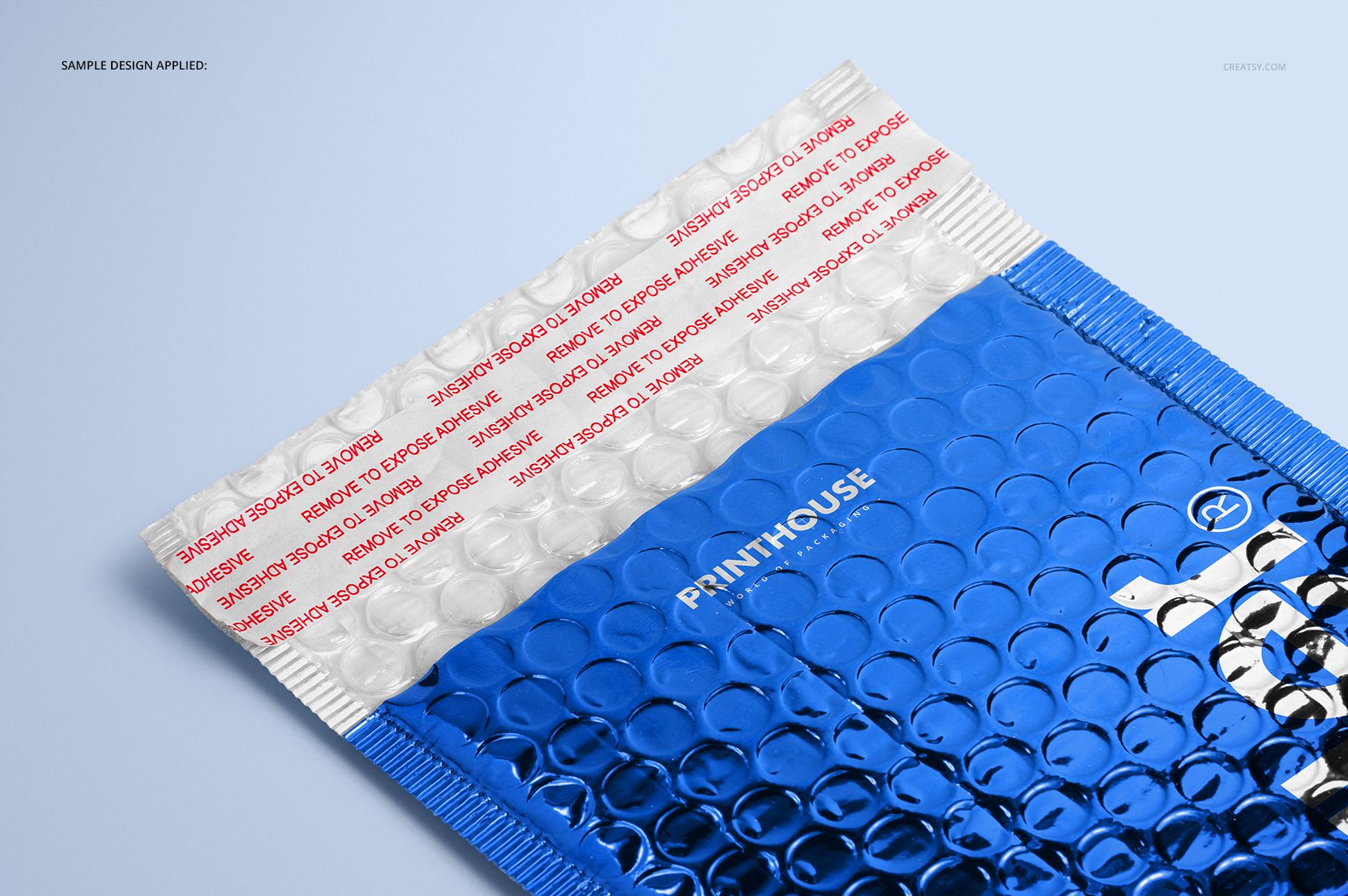 Blue metallic bubble mailer mockup with a white sealing strip, displayed at an angle on a pale surface.