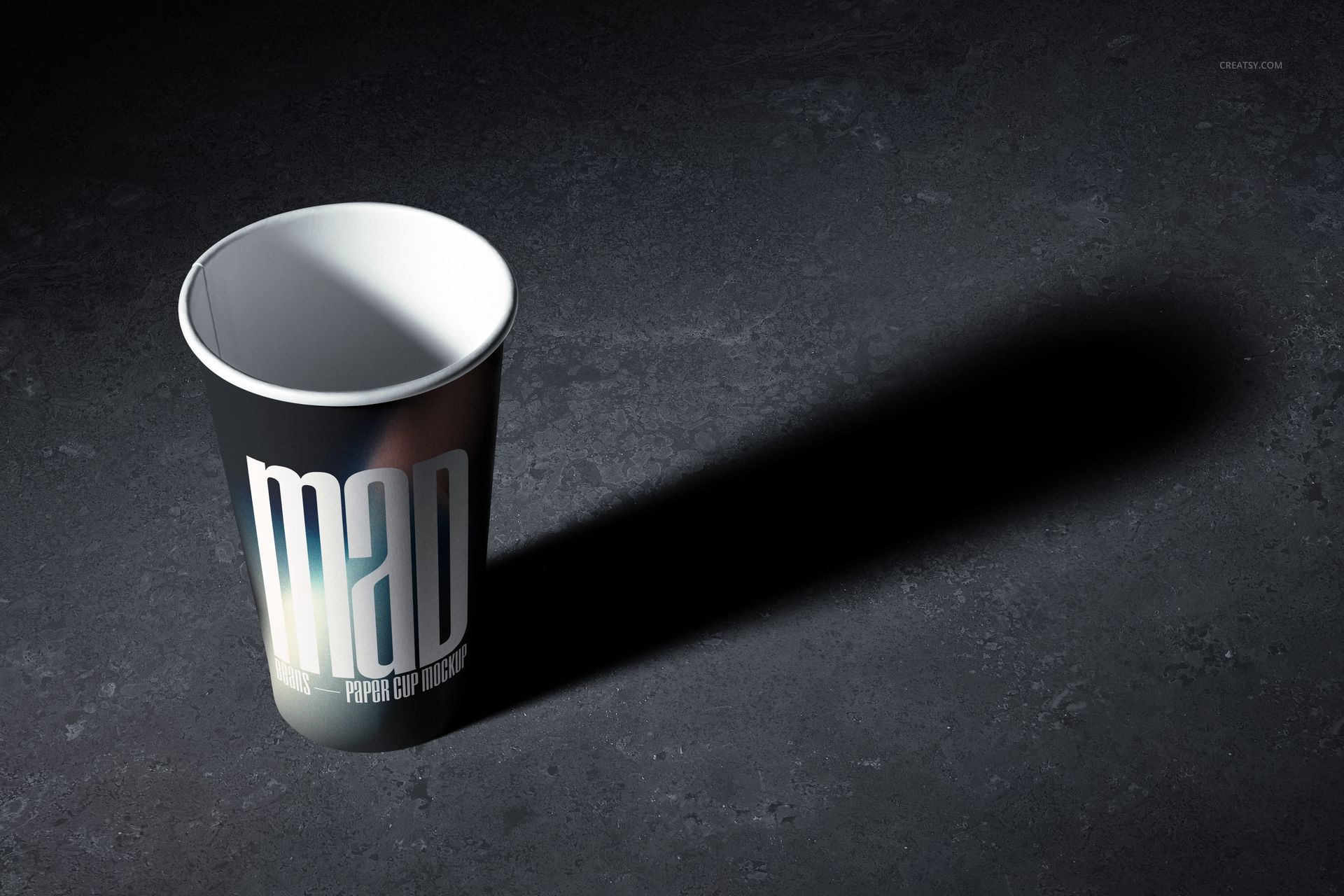 PSD mockup featuring a paper cup with a dark design and prominent text, illuminated and casting a shadow on stone-like ground.