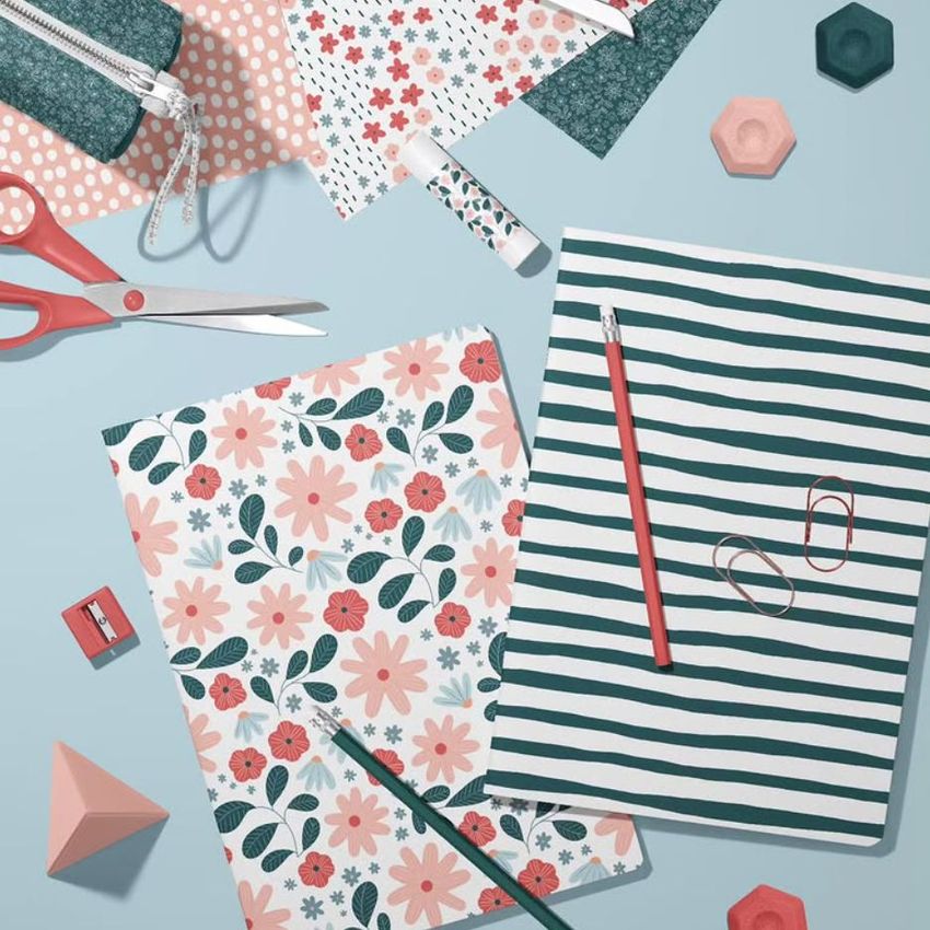 Stationery mockup featuring two A4 notebooks, one with pink floral patterns and one with green stripes, surrounded by office supplies.